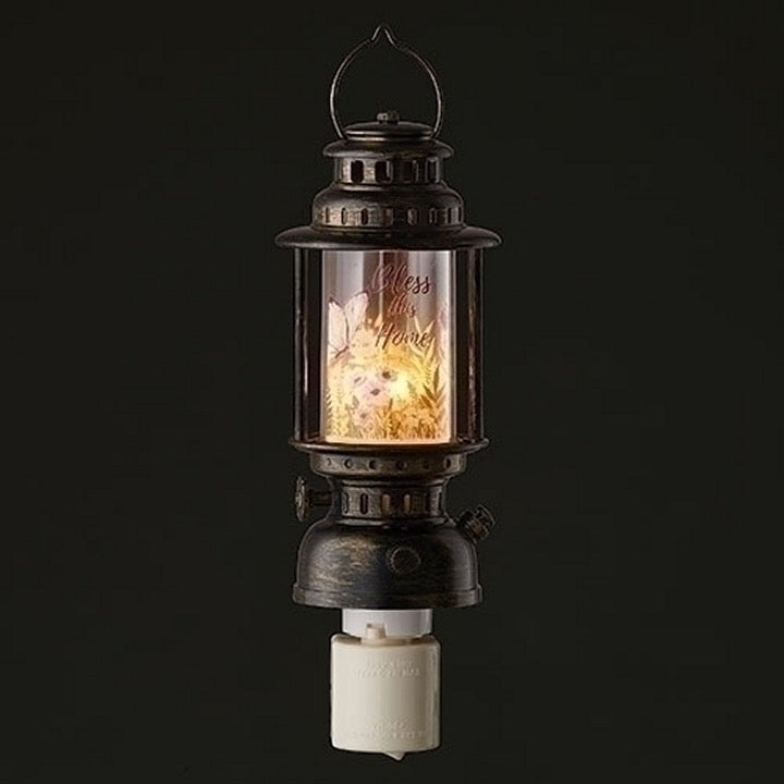 Illuminate your home with the stunning Bronze Look Lantern Night Light from Roman. Featuring a clear shade adorned with butterflies, purple flowers, and greenery, this night light adds a touch of beauty to any room. With "Bless This Home" written across the shade, it's not just a pretty face - it also provides a sweet sentiment. Measuring 8 inches in height and 2.5 inches in width, this night light is both decorative and practical.