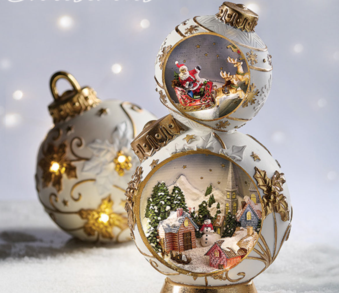 Illuminate your holiday decor with our LED Christmas Scene figurine. This extraordinary piece features two Christmas balls in white and gold, each with LED lights shining from within. The detailed Christmas scenes include a snowman & Christmas village on bottom with Santa on top. With natural flaws adding a vintage touch and gold holly patterns, this ornament is sure to add a festive touch to your home.