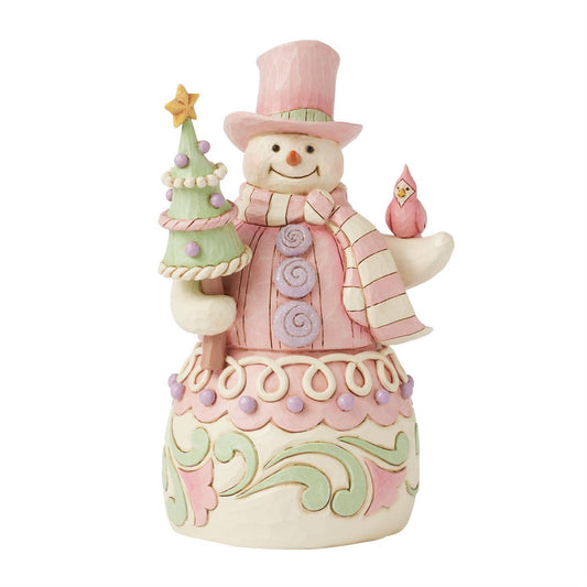 This whimsical Heartwood Sweets pastel pink snowman by Jim Shore radiates charm with his rosemaling patterns, sprinkles, and icing details, embodying the essence of holiday cheer. He lovingly holds a decorated tree and a cardinal.